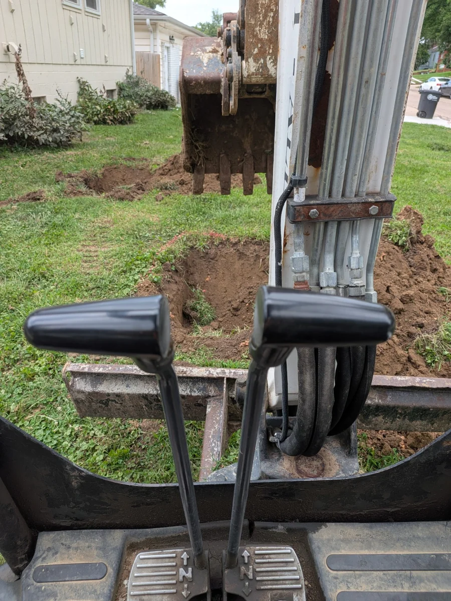 Excavator working beside a home during an underground pipe project