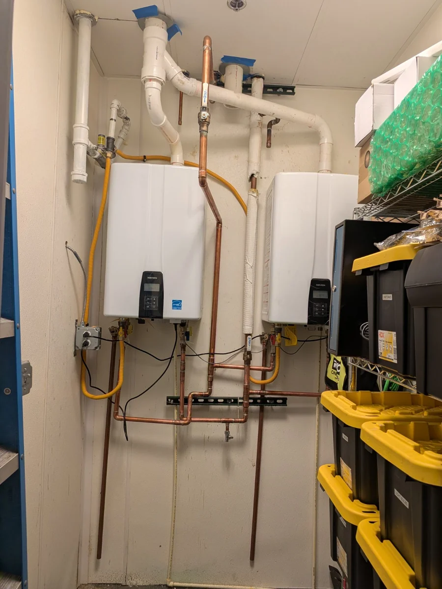 Two wall-mounted tankless water heaters with copper piping and vent connections